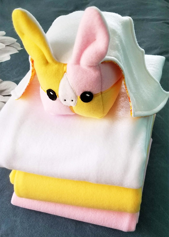 Bat-enberg Cake plush toy sitting on a stack of fleece fabric