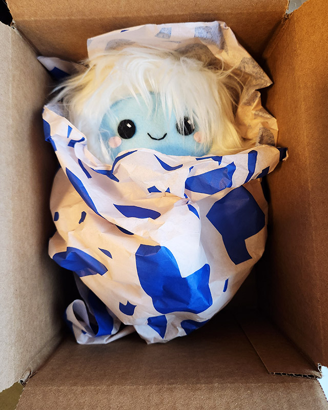 Fuzzy Yeti plushie swaddled in pink and blue gift wrap