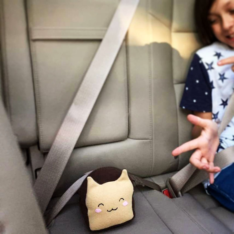 Meow-Bao the Catloaf plushie sitting with a seatbelt on and a happy kid